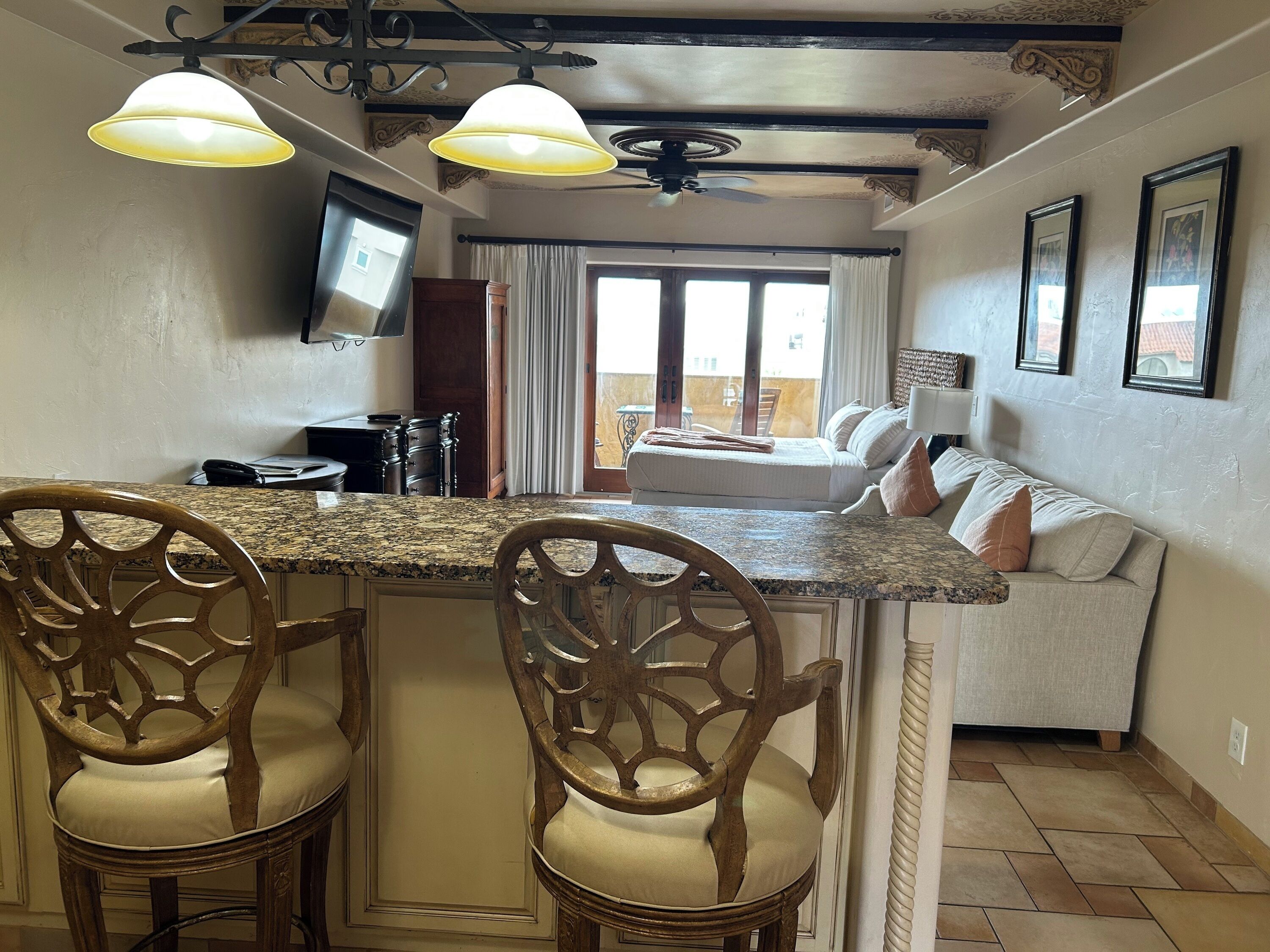 A kitchen with a granite countertop, two wooden chairs, a ceiling fan, and a dining area with a sofa.
