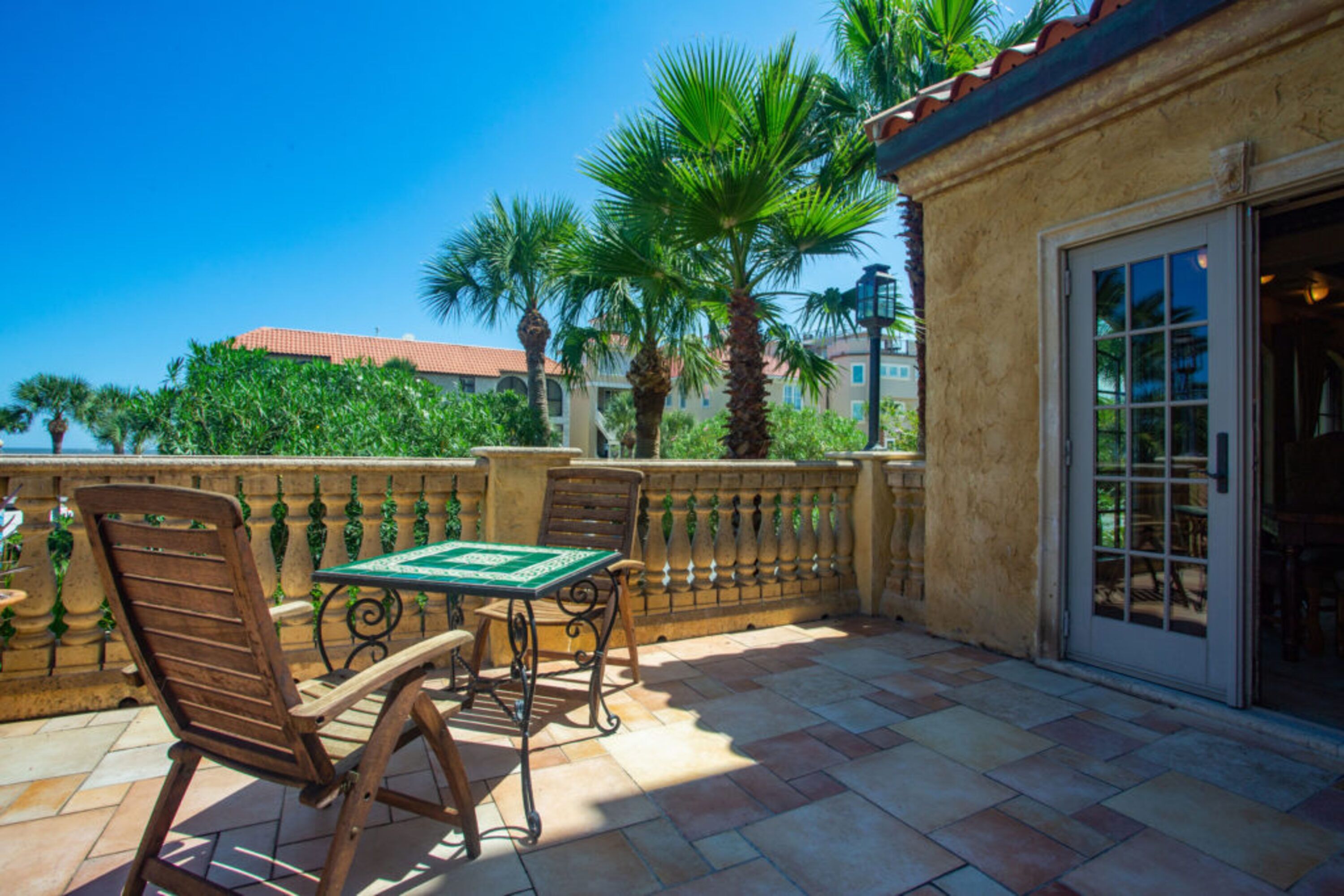 A patio with a table and chairs, a stone wall, and palm trees.
