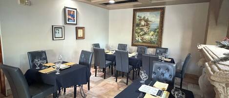 A dining area with a high ceiling, a chandelier, framed pictures on the walls, and a tiled floor.