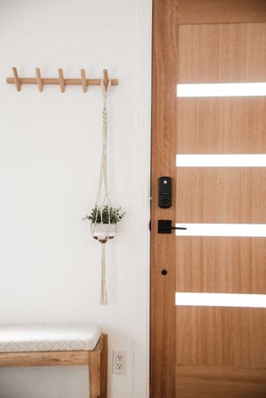 Une porte en bois avec un trou de serrure et une serrure, un mur blanc orné d’un porte-manteau en bois, et une plante en macramé suspendue.