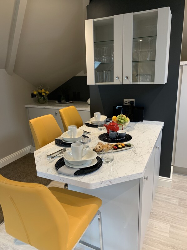 A modern kitchen with a marble countertop, yellow chairs, and a built-in cabinet above the island.