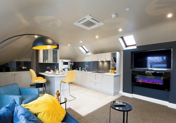 A modern living room with a blue sofa, a yellow pillow, a small table, and a TV. - Luxurious one bed apartment (Killarney)