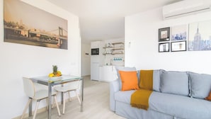 A modern living room with a grey sofa, a glass dining table, and a kitchen in the background. - Home2Book Design Las Canteras2 Beach (Las Palmas de Gran Canaria)