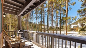 A wooden deck with a railing, wooden chairs, and a snow-covered ground.