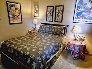 A bedroom with a bed, two nightstands, a lamp, decorative wall art, and a poster.