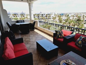 A balcony with red and black furniture, a tiled floor, and a view of a residential area with palm trees and buildings.