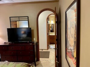A bedroom with a TV on a dresser, a door leading to a bathroom, and a poster on the wall.
