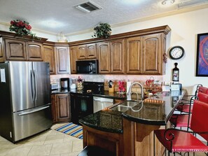 A kitchen with wooden cabinets, stainless steel appliances, a granite countertop, and a red chair.