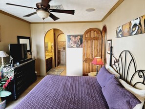 Une chambre à coucher avec un lit, un ventilateur de plafond, une commode, un téléviseur et un tableau représentant un tigre.