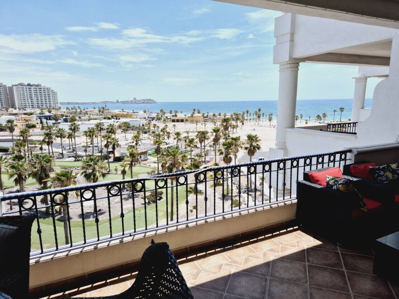 Un balcone con vista su una spiaggia, palme e un skyline lontano.