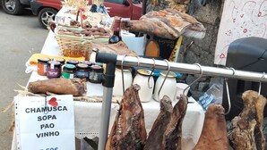 Un étal de marché proposant divers produits alimentaires, dont une affiche indiquant « CHAMUSCA SOPA PAO VINHO » au prix de 7,50 €.