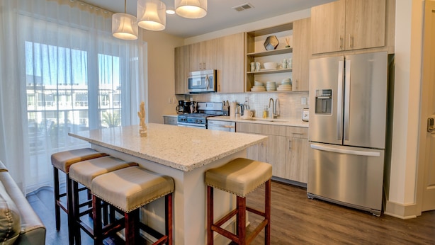 A modern kitchen with a central island, bar stools, stainless steel appliances, and wooden cabinetry. - The Pointe on 30A. Included 2 chairs with 1 umbrella beach set up + 2 bikes (Inlet Beach)
