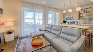 A modern living room with a leather sofa, a small wooden table, and a kitchen area with a microwave and cabinets. - The Pointe on 30A. Included 2 chairs with 1 umbrella beach set up + 2 bikes (Inlet Beach)