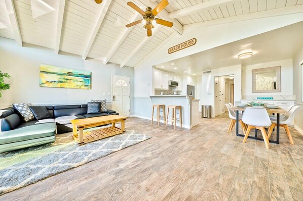 A spacious living area with a sofa, coffee table, and a dining table with chairs. A kitchen is visible in the background.