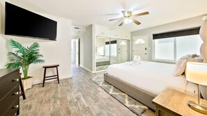 A modern bedroom with a large bed, a ceiling fan, a flat-screen TV, a potted plant, and a small stool. - Perfect 3 Bedroom Home between the Bay and Beach (Newport Beach)