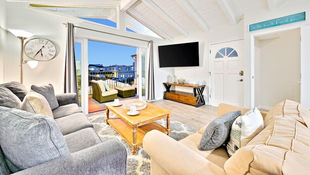 A modern living room with a large window, a flat-screen TV, and a cozy seating area. - 6 Bedroom Home with Rooftop Deck Between the Bay & the Beach (Newport Beach)