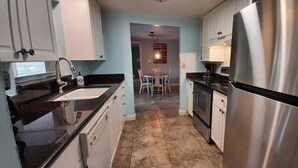 A modern kitchen with stainless steel appliances, a sink, and a dining area in the background. - Artist owned home near beaches (Venice)