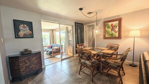 A dining area with a glass table and wicker chairs, a dark wooden cabinet, and a painting of a tiger on the wall. - Artist owned home near beaches (Venice)