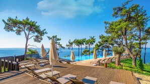 Un pontile di legno con poltrone relax e ombrelloni che si affaccia su un mare cristallino e blu.