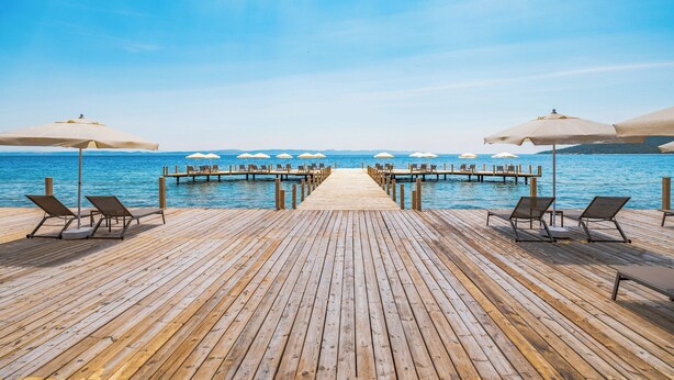 Un molo in legno conduce a una piscina con lettini e ombrelloni.