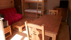 Ett litet rum med en våningssäng, ett träbord och en röd soffa.