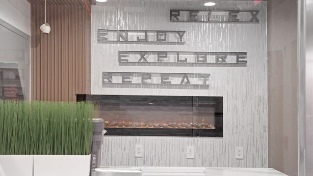 Un interior modern amb una llar de foc, un panell de fusta vertical i un rètol amb la frase 'REX ENJOY EXPLORE HEAT'.