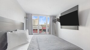 Habitació d'hotel moderna amb un llit gran, televisió de pantalla plana penjada a la pared i vista a la ciutat a través de grans finestres.