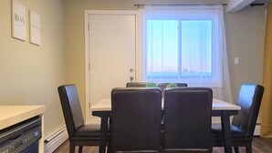 Un comedor pequeño con una mesa, sillas, una ventana con cortinas translúcidas y una puerta.