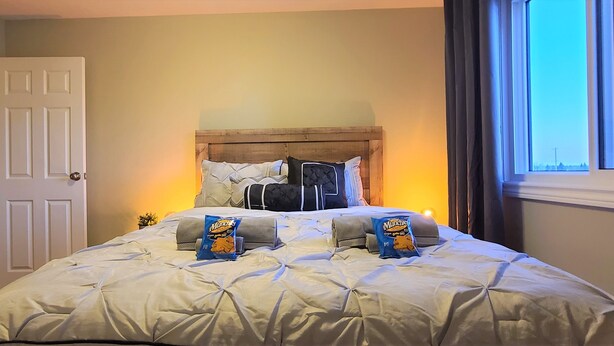 Una cama bien hecha con cabecera, dos almohadas y dos paquetes de aperitivos Munchies.