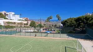 A sports court with a goalpost, surrounded by a fence, and a view of buildings and palm trees in the background.