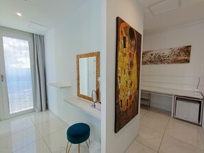A modern bathroom with a large mirror, a sink, and a toilet. There is a blue stool and a decorative painting on the wall.
