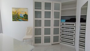 A room with a white cabinet with multiple drawers, a chair, and a painting on the wall.