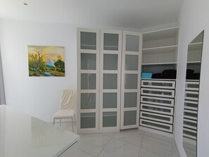 Une pièce avec un meuble blanc doté de nombreux tiroirs, une chaise et un tableau accroché au mur.