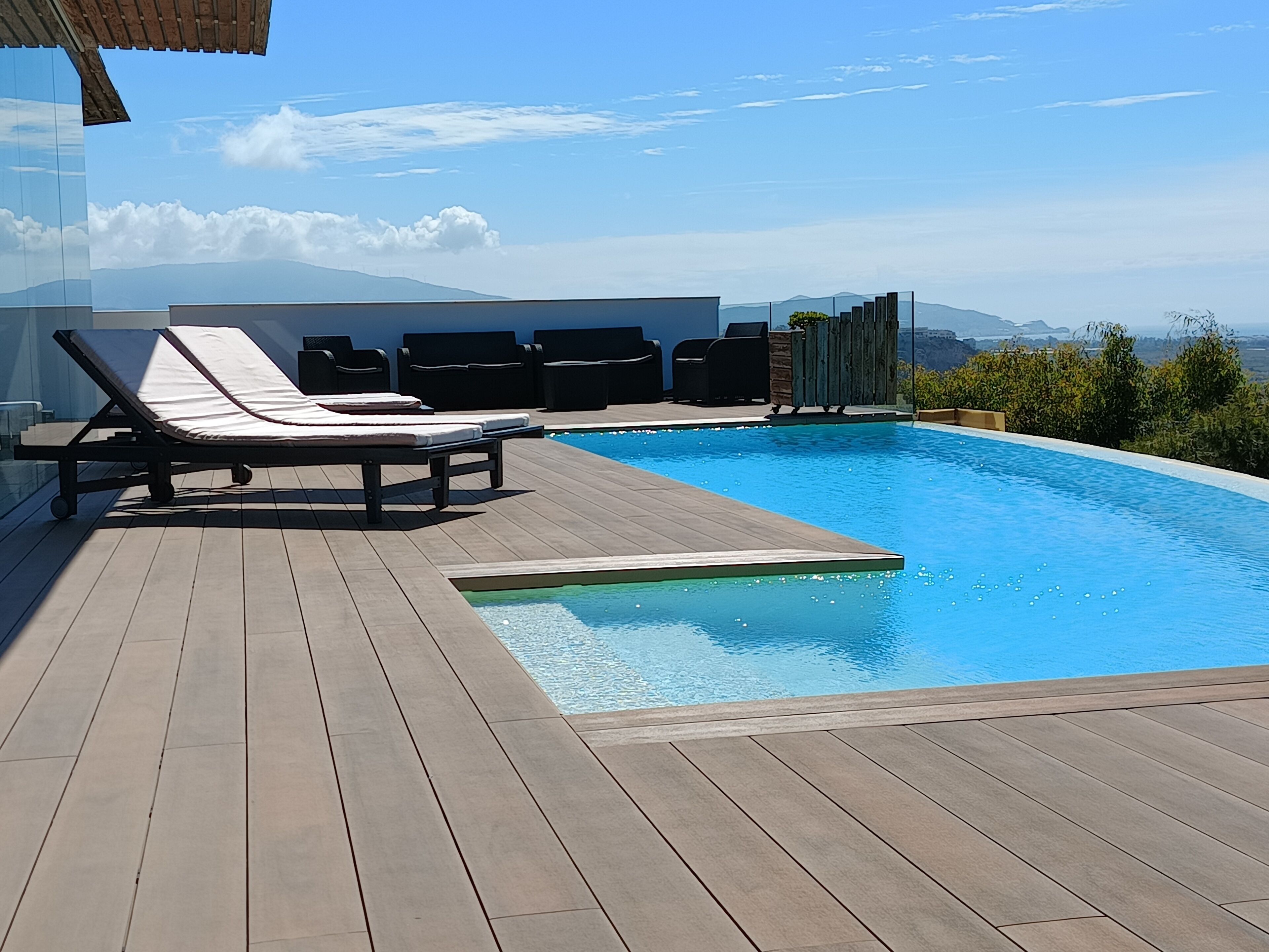 A swimming pool with lounge chairs and a deck, surrounded by a clear sky and distant mountains.