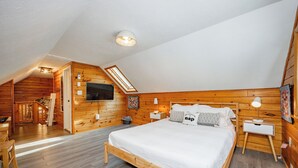 Une chambre confortable située sous les toits, avec un plafond en pente en bois, un grand lit, un bureau et un téléviseur fixé au mur.