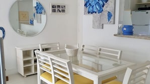 A dining area with a white table and chairs, a round mirror, and artwork on the wall.