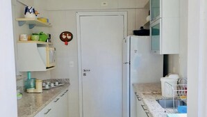 A compact kitchen with white cabinets, a refrigerator, a stove, and a microwave. There is a green striped rug on the floor.