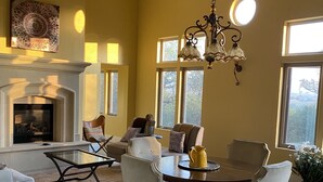 Un salon spacieux doté d’une cheminée, un coin repas avec une table ronde et des chaises, et de grandes fenêtres laissant entrer la lumière naturelle.