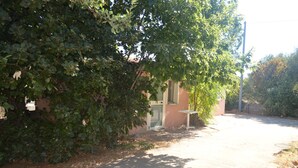 A paved driveway leading to a building with a door and a small table. - Pink House (Sardegna)