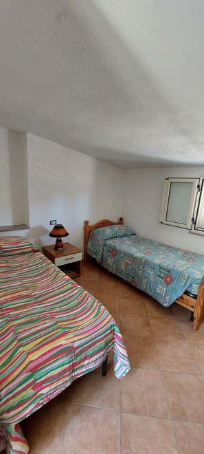 A small, single-room accommodation with two beds, a nightstand, a lamp, and a wardrobe.