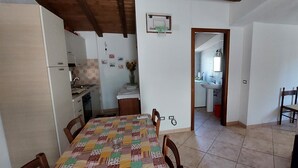 A dining area with a table covered in a patchwork tablecloth, wooden chairs, and a kitchen in the background. - Pink House (Sardegna)