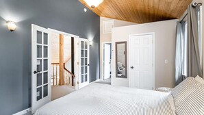 A bedroom with a large bed, a wooden ceiling, and a view of a bathroom. - Cottage in the Woods (Seward)