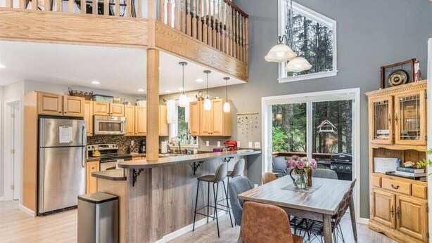 A modern kitchen with wooden cabinets, stainless steel appliances, and a central island with bar stools. - Cottage in the Woods (Seward)