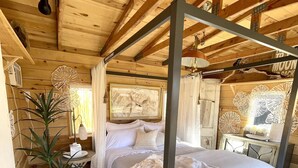 A wooden cabin bedroom with a four-poster bed, a potted plant, and a wall-mounted fan. - Mill Street Station bungalow 10 minutes to Zion (Virgin)