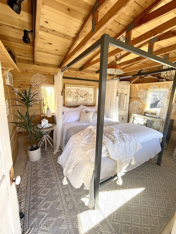 Ein Schlafzimmer einer Holzhütte mit einem Himmelbett, einer Topfpflanze und einem Wandventilator.