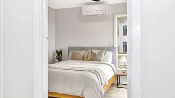 Une chambre à coucher avec un lit, une table de chevet, une lampe et une vue sur l’extérieur.