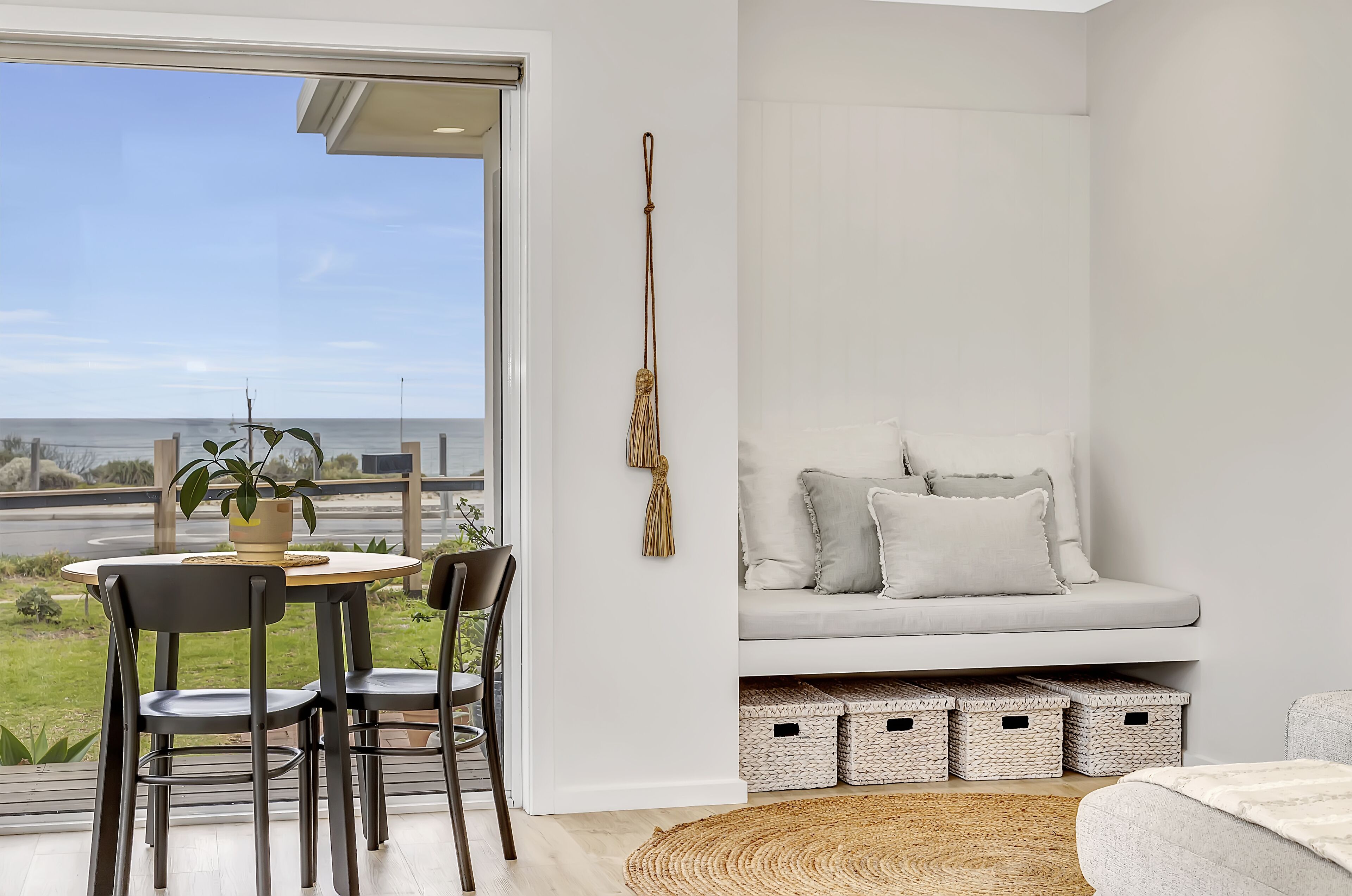 Uma sala de estar moderna com sofá, mesa de jantar com cadeiras, vista para o oceano e cestos organizadores.