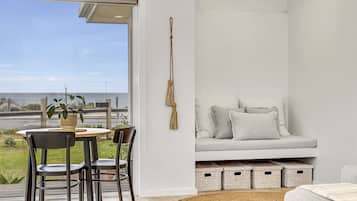 Uma sala de estar moderna com sofá, mesa de jantar com cadeiras, vista para o oceano e cestos organizadores.