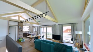 A spacious living room with a large teal sofa, wooden beams on the ceiling, a television, and a dining area with a table and chairs. - Eco-Chalet Matschiedl
Luxury mountainside Eco Chalet with stunning view -  (Kärnten)