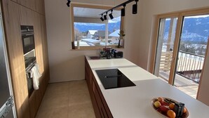 A modern kitchen with a large island, wooden cabinets, and a view of mountains through the windows. - Eco-Chalet Matschiedl
Luxury mountainside Eco Chalet with stunning view -  (Kärnten)